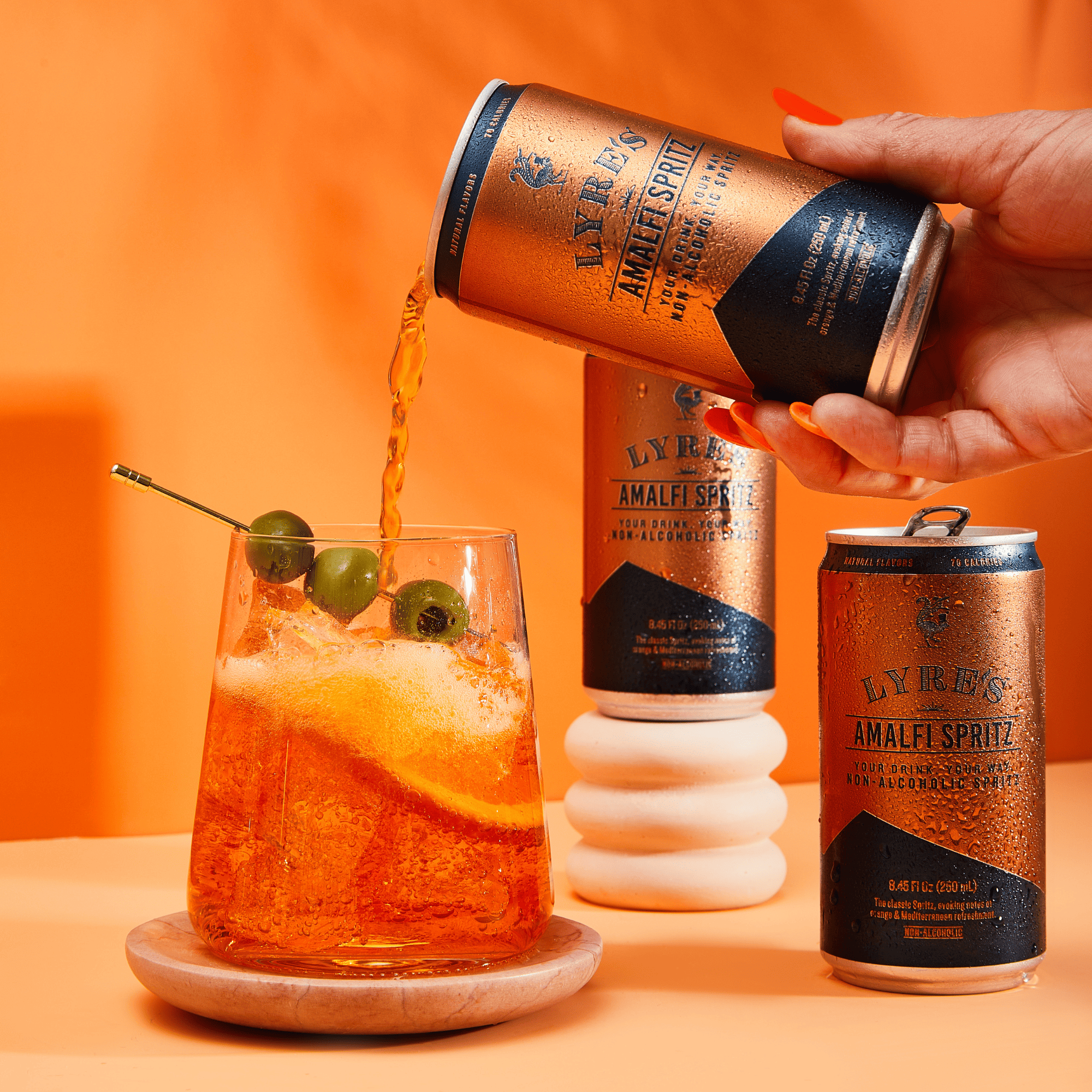 Person pouring Lyres Non Alcoholic Amalfi Spritz into a glass with an orange background