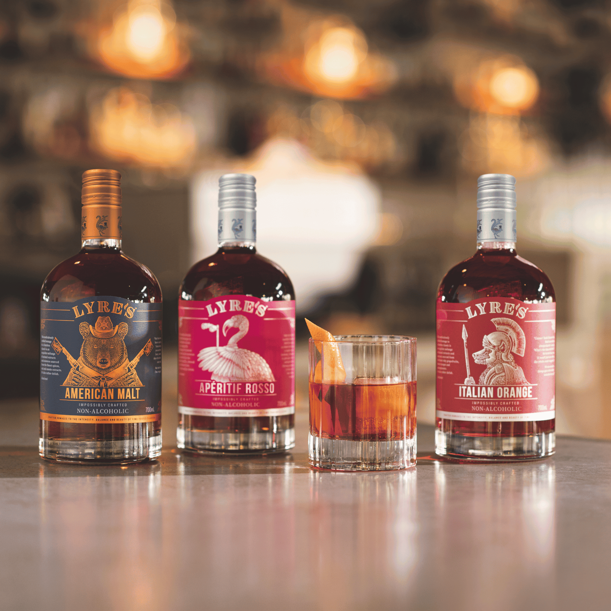 Three bottles of Lyre's American Malt, Aperitif Rosso and Italian Orange, accompanied by a glass of non alcoholic cocktail.