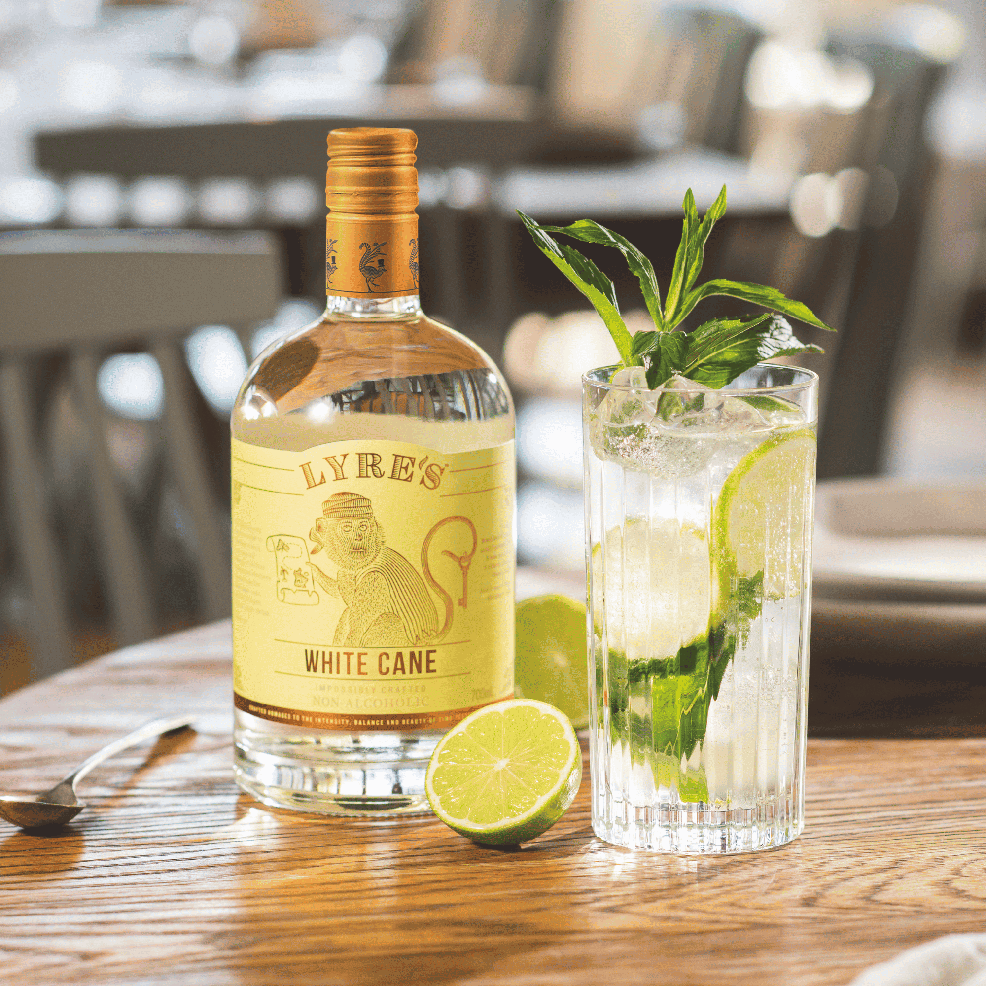 Lyre's White Cane bottle with a mojito garnished with lime and mint on a wooden table.
