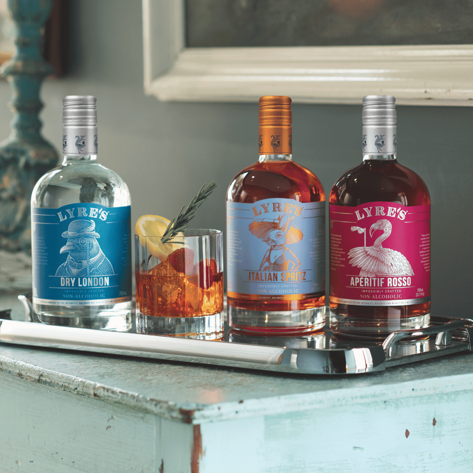 Three bottles of Lyre's Dry London, Italian Spritz and Aperitif Rosso on a tray with a non alcoholic cocktail in the center.